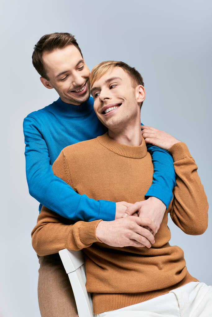 Dois homens elegantes, um casal gay amoroso, sentam-se juntos em um pano de fundo cinza. - Foto, Imagem