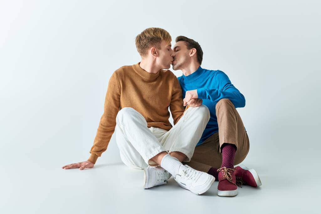 Zwei junge Männer in legerer Kleidung sitzen auf dem Boden und küssen sich. - Foto, Bild