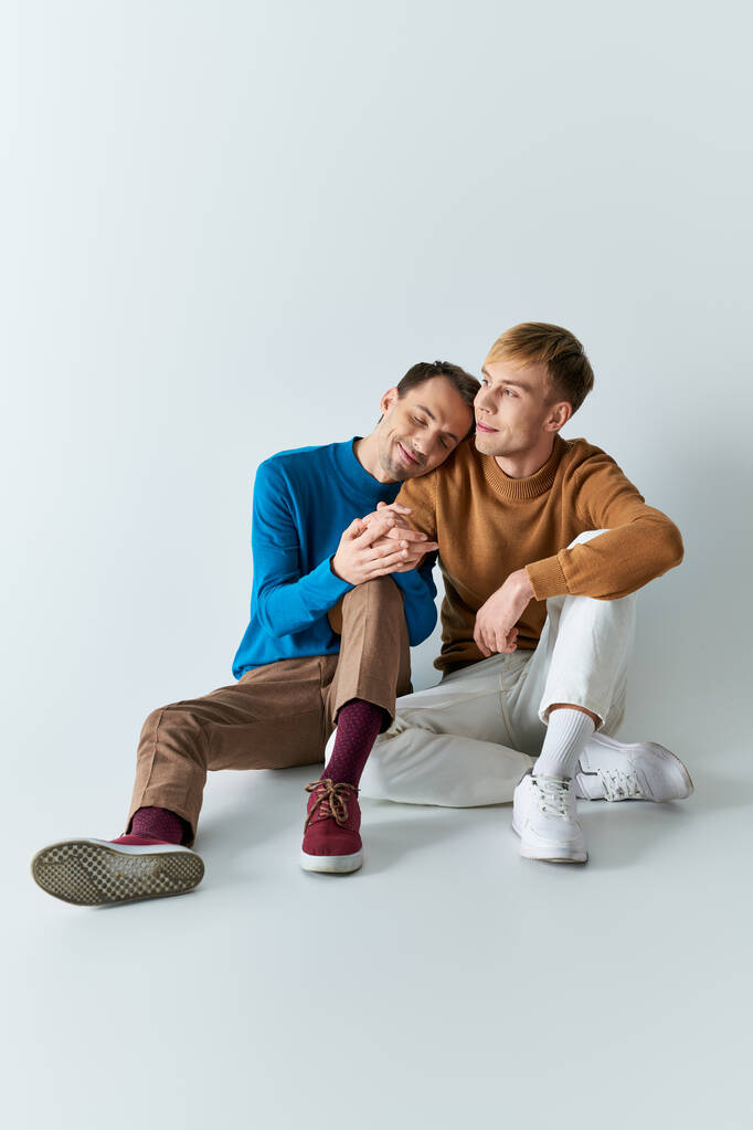 Kaksi miestä, rakastava homopari, istumassa vierekkäin rennossa asussa harmaalla taustalla.. - Valokuva, kuva