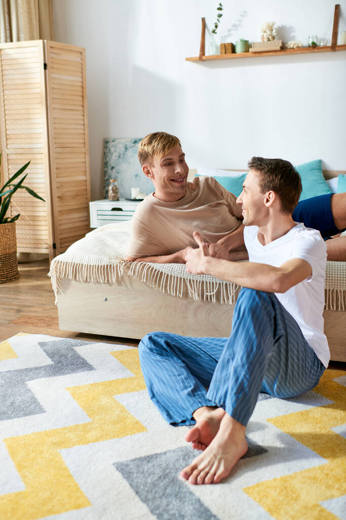 Dos hombres, una pareja gay amorosa, se sientan con gracia en la parte superior de un sofá en atuendo casual, disfrutando de la compañía de los demás. - Foto, Imagen