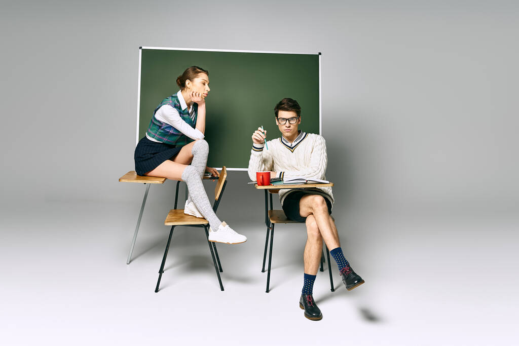 Knappe man en stijlvolle vrouw zitten voor een schoolbord in een college setting. - Foto, afbeelding
