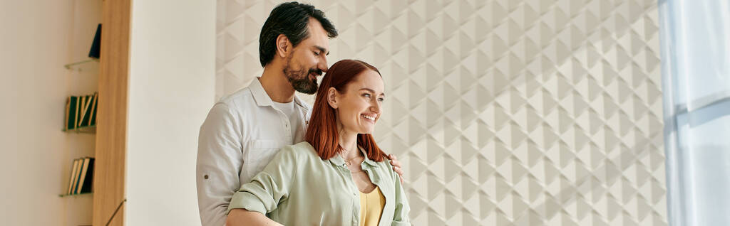 Uma mulher ruiva elegante e um homem barbudo estão juntos em frente a uma parede da moda em um apartamento moderno. - Foto, Imagem