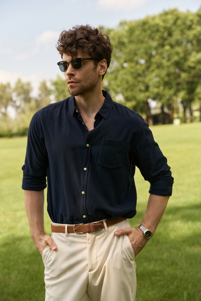 Egy elegáns férfi tengerészeti ingben és napbarnított nadrágban, kecsesen áll egy zöld mezőn.. - Fotó, kép