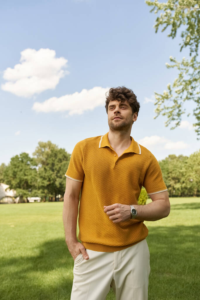 Чоловік у яскраво-жовтій сорочці поло елегантно стоїть у пишному зеленому полі під теплим ранковим сонцем. - Фото, зображення