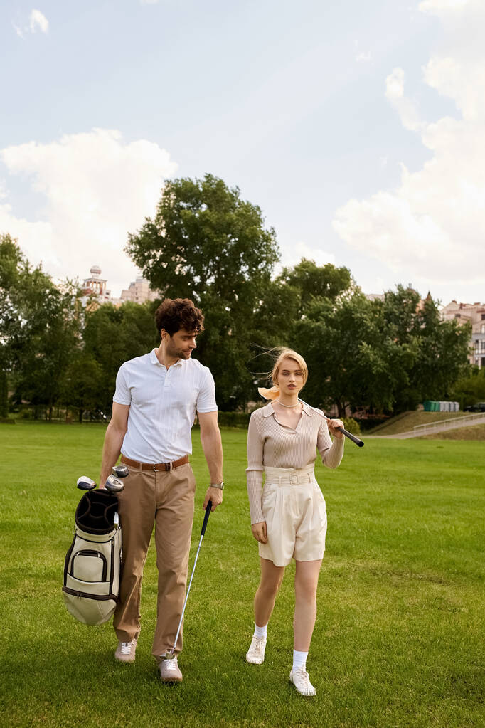 Tyylikäs pari tyylikkäässä puvussa kävelemässä yhdessä rehevällä vihreällä golfkentällä avoimen taivaan alla. - Valokuva, kuva