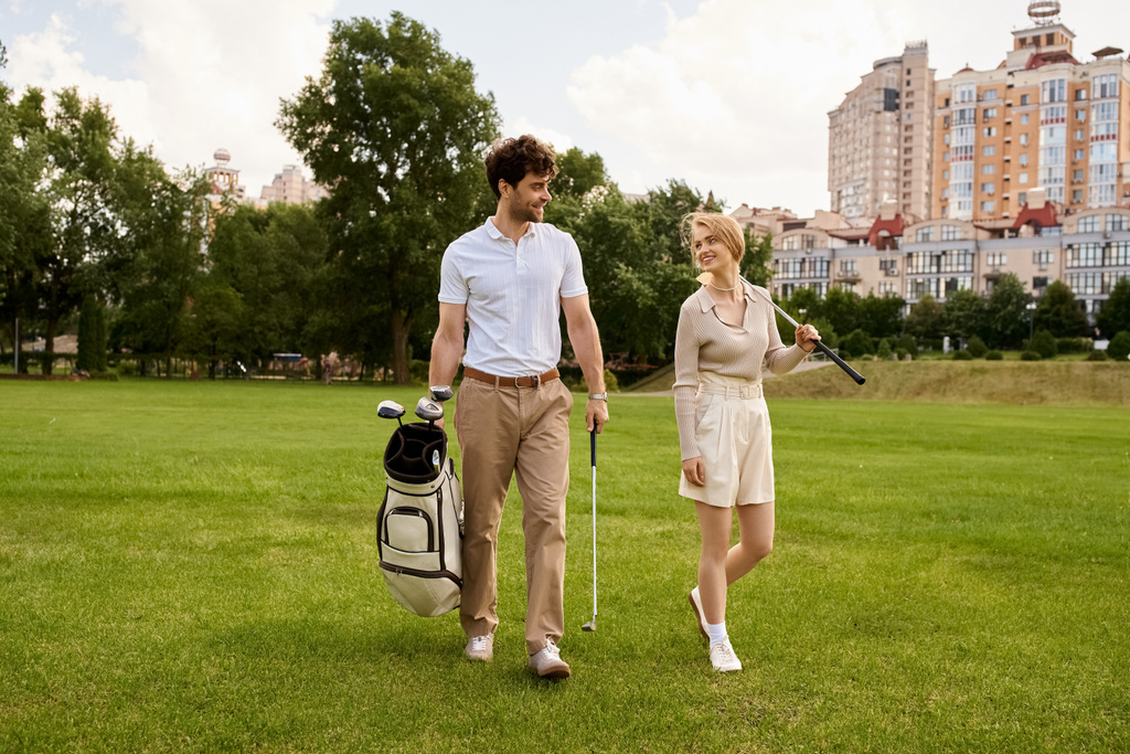 Egy fiatal pár elegáns öltözékben kényelmesen átsétál egy buja zöld golfpályán, élvezve egy luxus szabadtéri élményt együtt. - Fotó, kép
