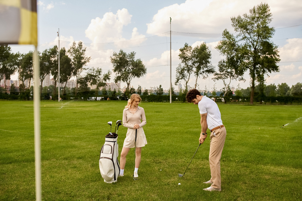 Şık giyinmiş genç bir adam ve kadın yemyeşil bir alanda golf oynuyorlar, golf kulübünde sakin bir günün tadını çıkarıyorlar.. - Fotoğraf, Görsel
