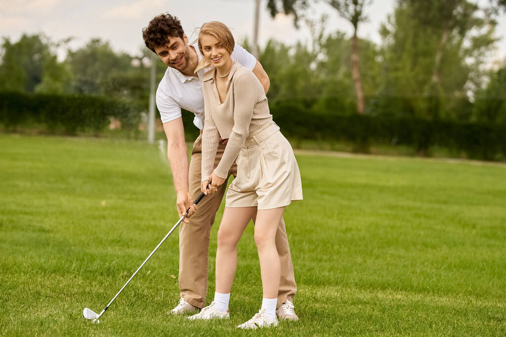 Mężczyzna i kobieta w eleganckim stroju grający w golfa na bujnym zielonym polu kija golfowego. - Zdjęcie, obraz