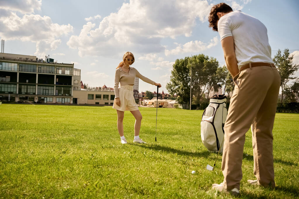 Młody mężczyzna i kobieta ubrani elegancko grają w golfa na bujnym zielonym polu, ciesząc się spokojnym popołudniem razem. - Zdjęcie, obraz