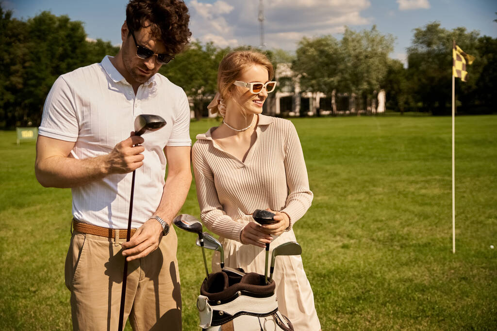 Nuori pari, tyylikkäästi pukeutunut, seisoo yhdessä viehättävällä golfkentällä, jossa on klassinen, yläluokan elämäntapa.. - Valokuva, kuva