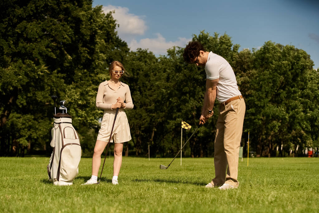 Una joven pareja en elegante atuendo disfruta de un juego de golf en un exuberante campo verde en un prestigioso club, encarnando el epítome del ocio de clase alta. - Foto, Imagen