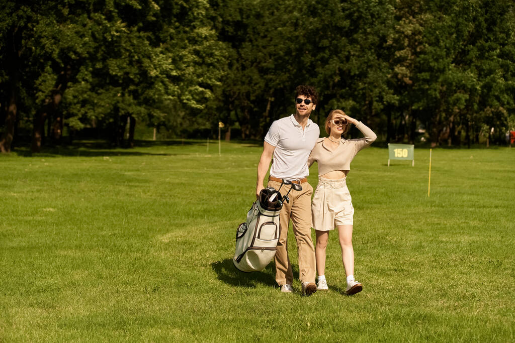 Stylowa młoda para spokojnie spaceruje po malowniczym polu golfowym, ciesząc się swoim towarzystwem. - Zdjęcie, obraz