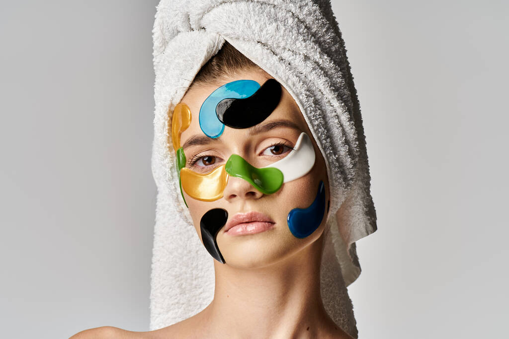 Μια νεαρή γυναίκα με μια πετσέτα τυλιγμένη γύρω από το κεφάλι της με κηλίδες ματιών στο πρόσωπό της. - Φωτογραφία, εικόνα