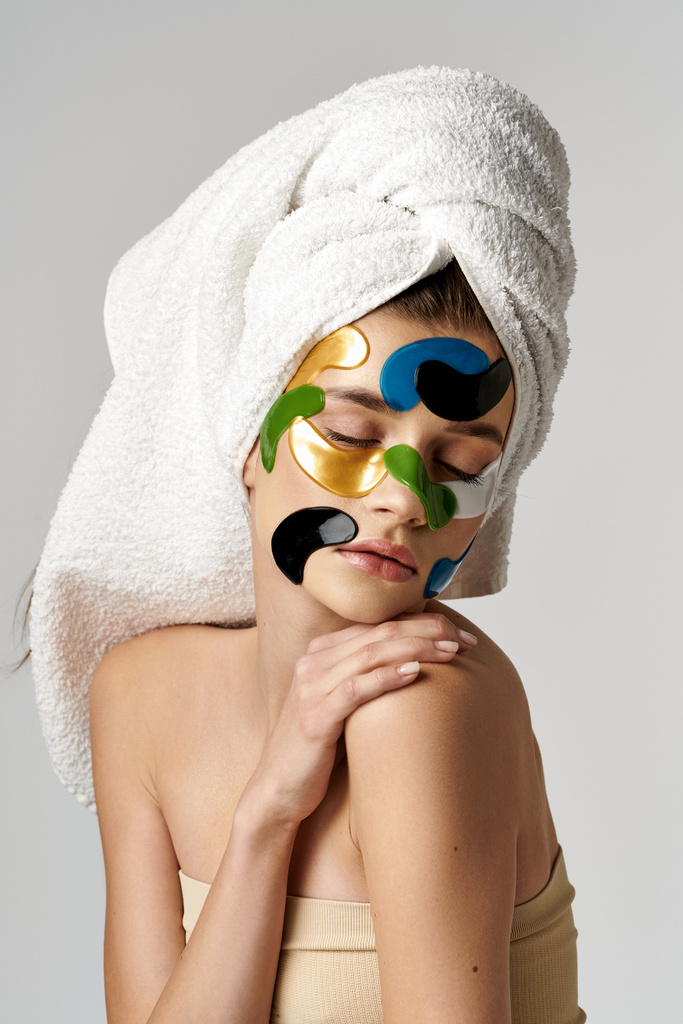 Μια γαλήνια γυναίκα που φοράει επιθέματα ματιών και πετσέτα στο κεφάλι της, ενδίδει σε μια χαλαρωτική ρουτίνα φροντίδας του εαυτού της. - Φωτογραφία, εικόνα