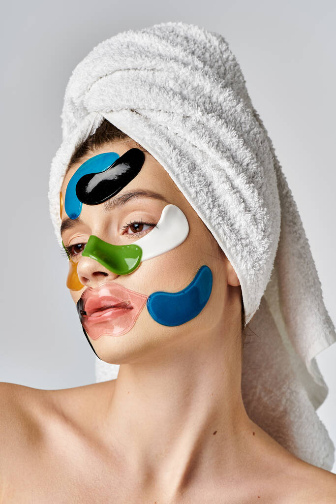 Μια γαλήνια νεαρή γυναίκα με κηλίδες ματιών στο πρόσωπό της και μια πετσέτα τυλιγμένη γύρω από το κεφάλι της θέτει χαριτωμένα. - Φωτογραφία, εικόνα