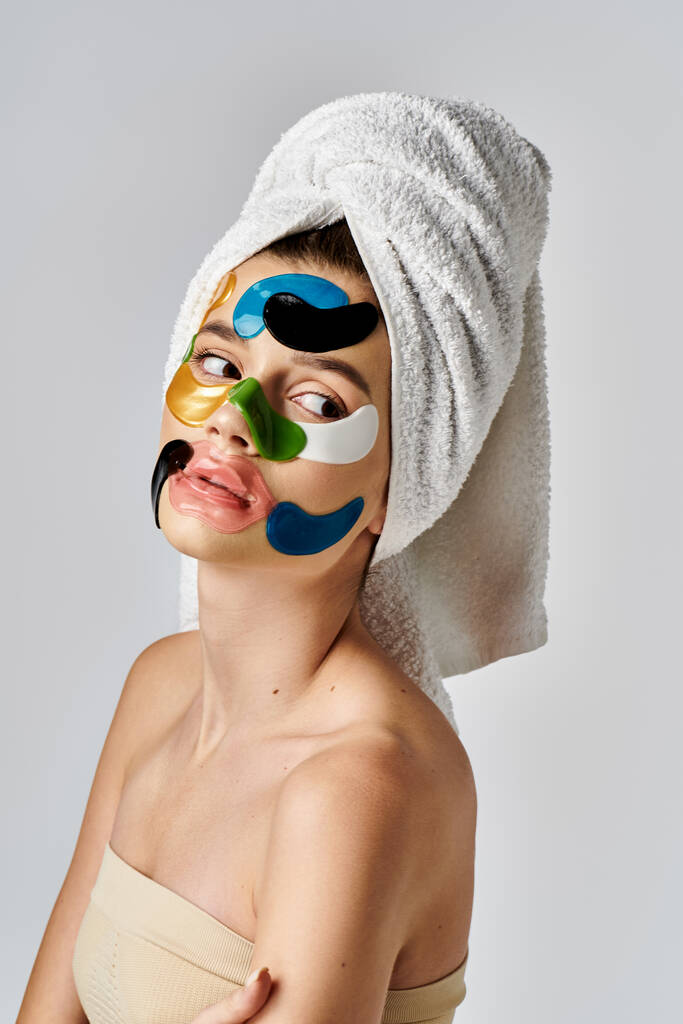 A beautiful young woman strikes a pose with a towel wrapped around her head and intricate eye patches. - Photo, Image
