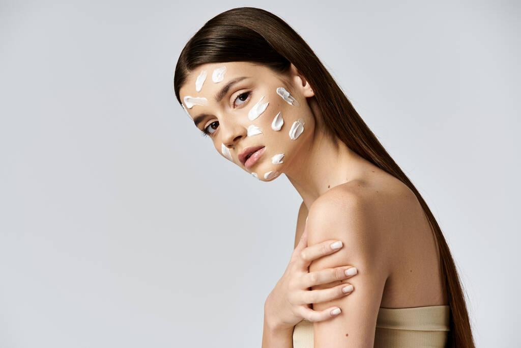 Eine schöne junge Frau posiert mit weißer Creme im Gesicht und unterstreicht ihre natürliche Schönheit mit Kosmetik. - Foto, Bild