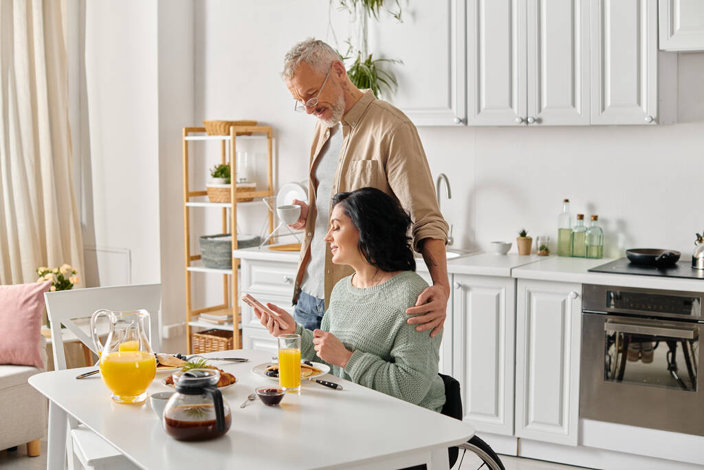 Чоловік і жінка з обмеженими можливостями в інвалідному візку разом у затишній кухні вдома, розділяючи теплий момент. - Фото, зображення