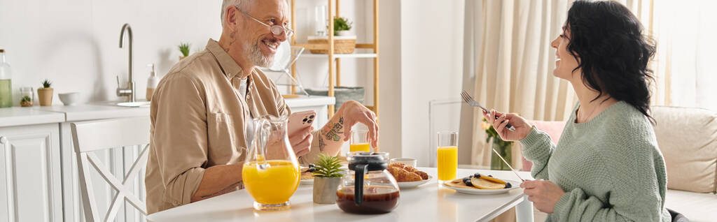 Un homme et une femme handicapée en fauteuil roulant partagent un repas paisible le matin à une table de cuisine confortable dans leur maison. - Photo, image