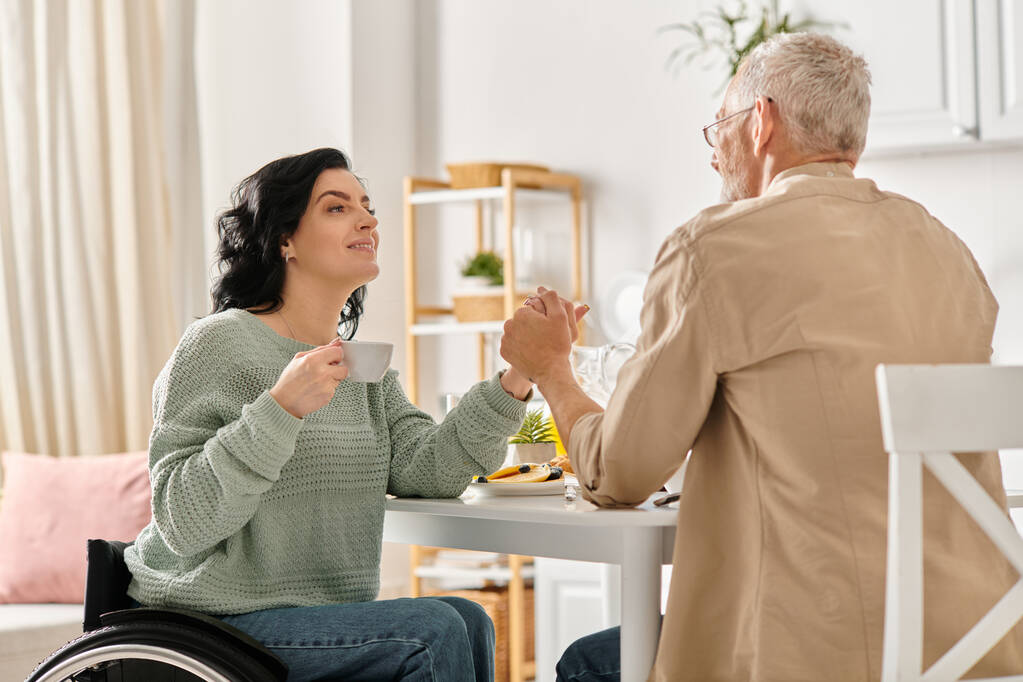 In een gezellige keuken thuis, een vrouw in een rolstoel hand in hand met haar man - Foto, afbeelding
