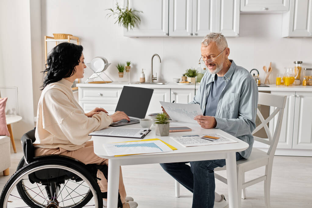 Una mujer en silla de ruedas conversa con un hombre en una acogedora cocina en casa, compartiendo un momento de conexión. - Foto, imagen