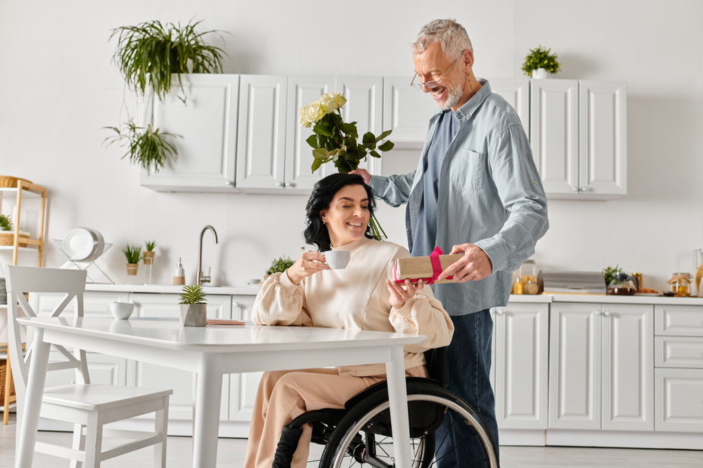 Ein Mann steht hingebungsvoll neben seiner behinderten Frau im Rollstuhl in der heimischen Küche. - Foto, Bild