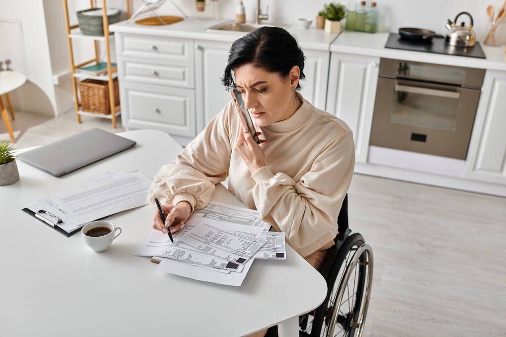 Una mujer discapacitada en silla de ruedas lee un papel mientras trabaja de forma remota desde su cocina. - Foto, imagen