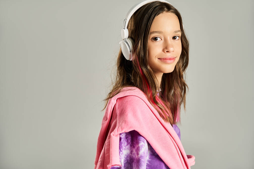 Ένα κομψό έφηβο κορίτσι φαίνεται γαλήνιο σε μια ζωντανή ρόμπα, ενεργά θέτουν, ενώ φορώντας ακουστικά. - Φωτογραφία, εικόνα