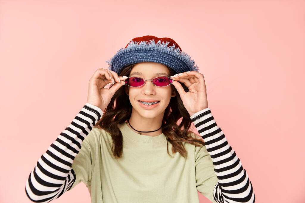 Tyylikäs teini tyttö iskee poseerata elinvoimainen puku, aurinkolasit ja hattu. - Valokuva, kuva