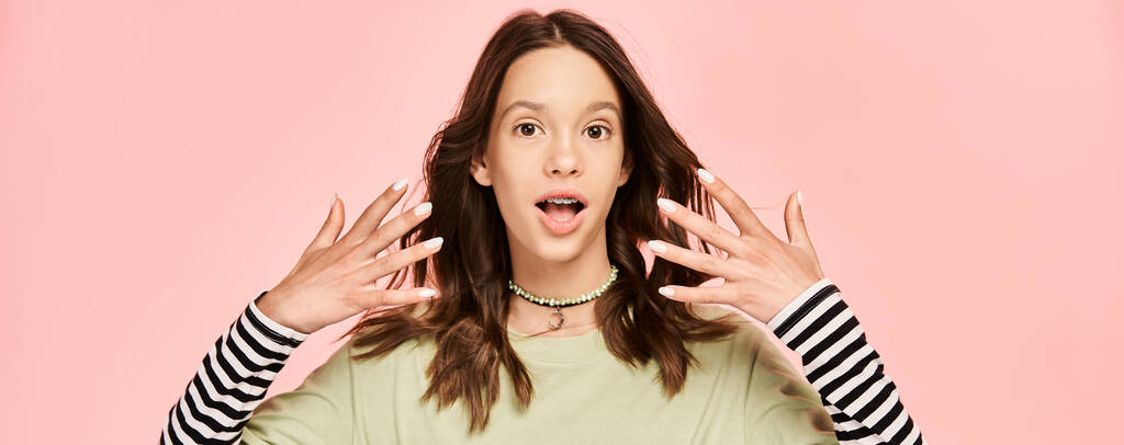Una adolescente vestida con un atuendo vibrante con las manos en alto frente a su cara, golpeando una pose dinámica. - Foto, imagen