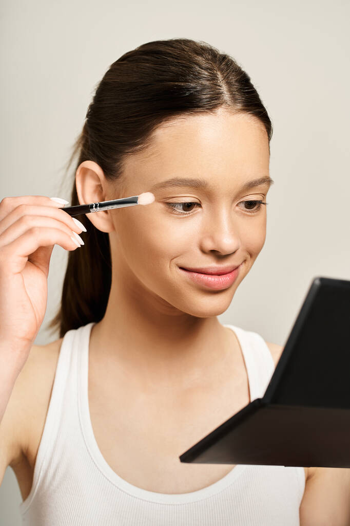 Una adolescente con estilo enérgicamente usando un cepillo para aplicar maquillaje en su propia cara, mostrando una forma divertida y artística de auto-expresión. - Foto, imagen