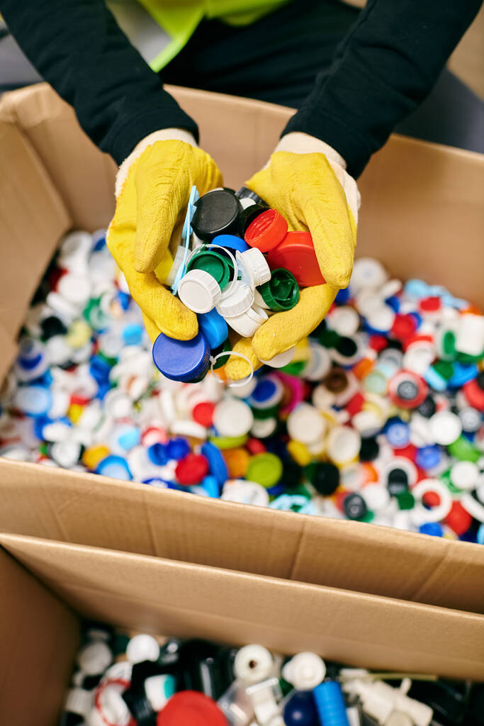 volunteer in yellow gloves carefully holding a bunch of colorful bottle caps - Foto, Bild
