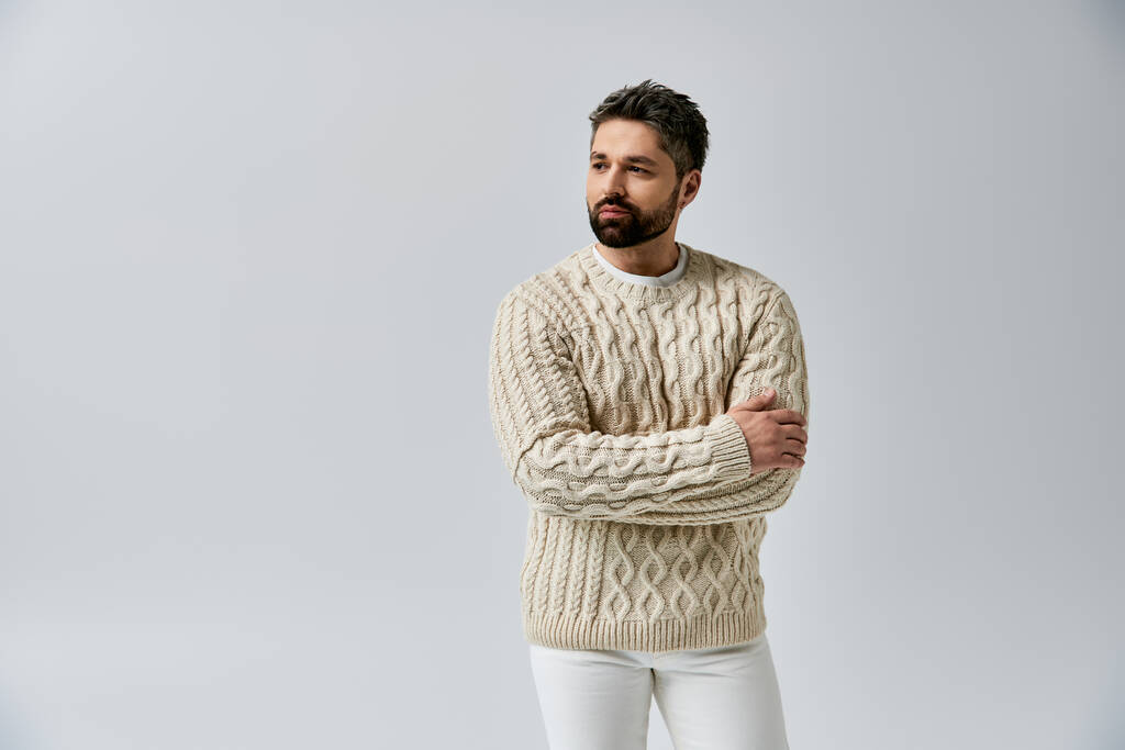 A stylish man with a beard striking a pose in a white sweater against a grey studio backdrop. - Photo, Image
