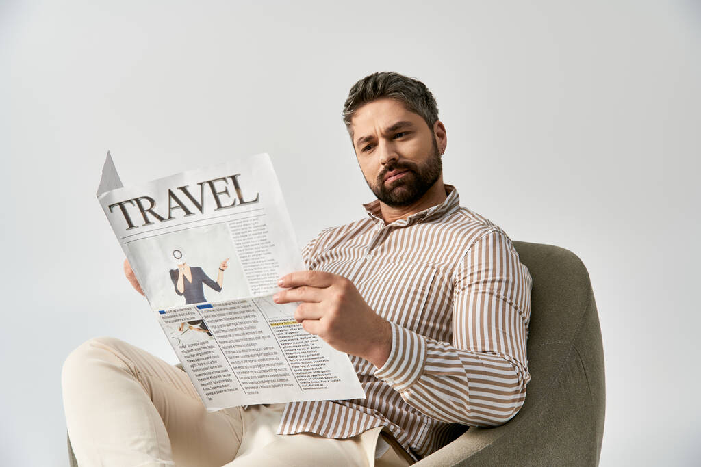 Stylový muž s vousy sedící v křesle zaujatý čtením novin, vyzařující sofistikovanost a šarm. - Fotografie, Obrázek