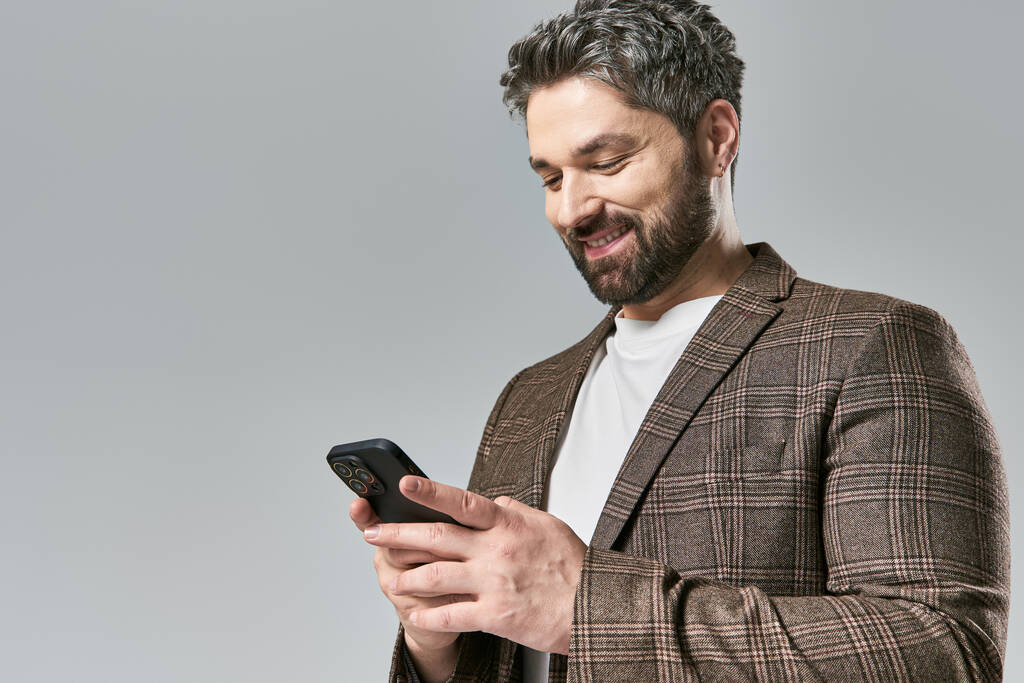 Een stijlvolle man in een pak staart aandachtig naar zijn mobiele telefoon, verzonken in gedachten. - Foto, afbeelding