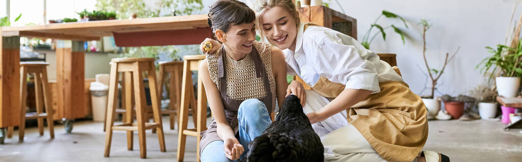 Two women in an art studio showing affection to a black hen. - Photo, Image
