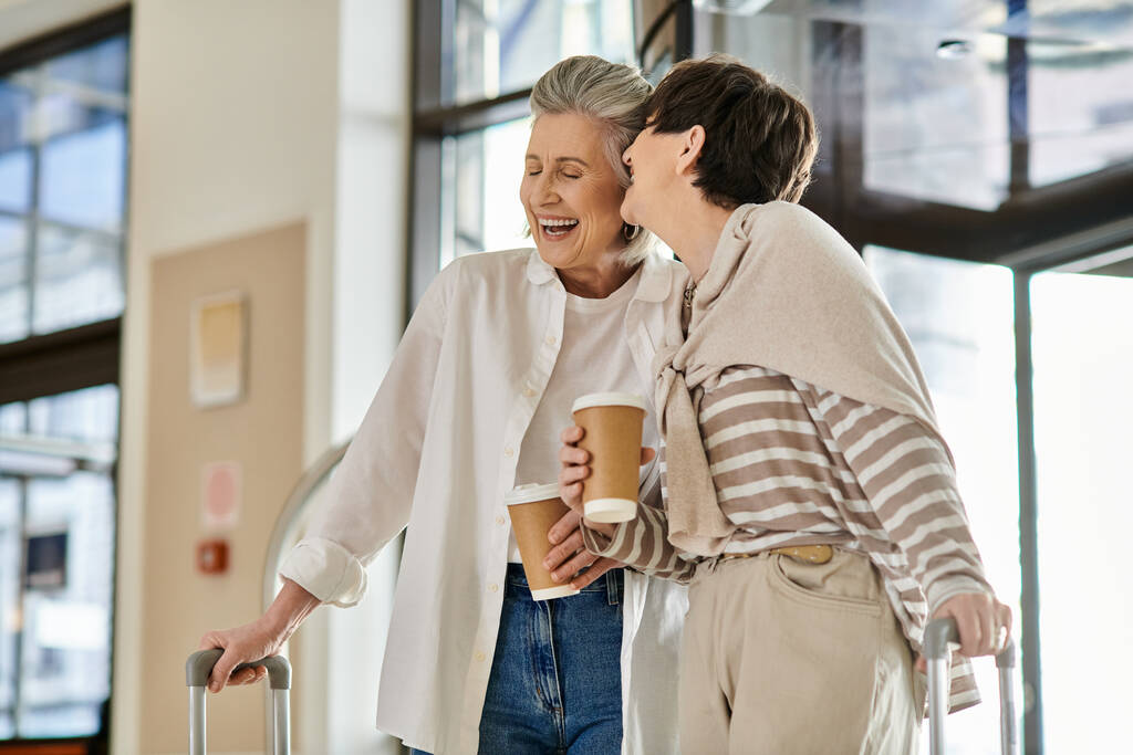 Two senior lesbian women holding luggage and sipping coffee. - Photo, Image