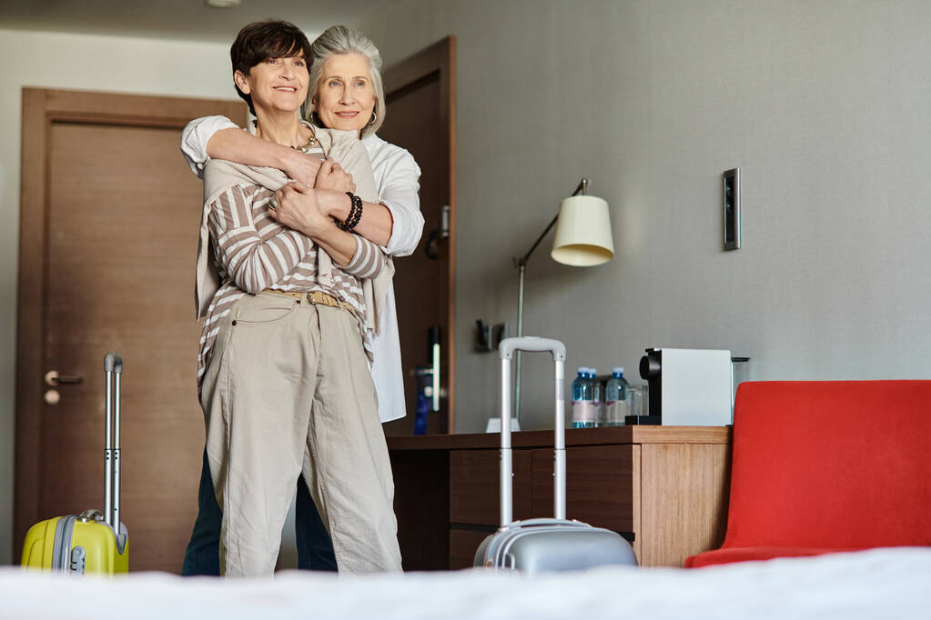 Senior lesbian couple share a tender hug in a luxurious hotel room. - Photo, Image