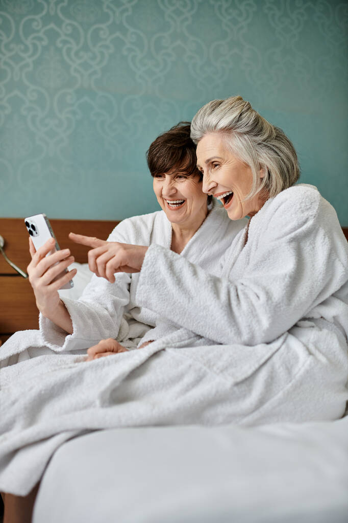 Zarte ältere lesbische Paar und junge Frau genießen Zeit zusammen auf einem Bett mit einem Mobiltelefon. - Foto, Bild