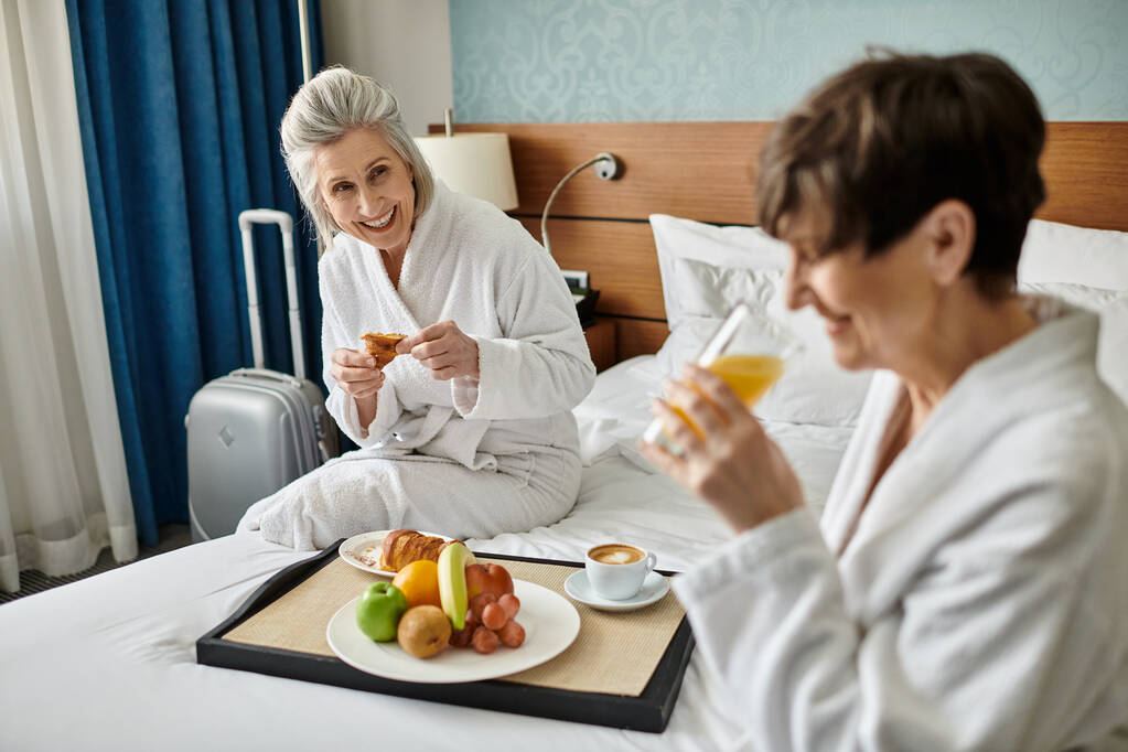 Dwie kobiety, kochająca starsza para lesbijek, siedząca czule spleciona na łóżku. - Zdjęcie, obraz