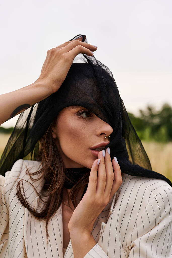 Une jeune femme en tenue blanche profitant de la brise estivale dans un champ, la tête ornée d'un voile délicat. - Photo, image