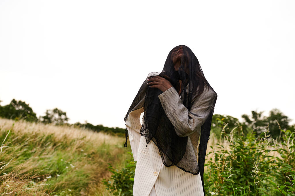 Μια νεαρή γυναίκα με λευκή ενδυμασία στέκεται με χάρη σε ένα χωράφι με ψηλό γρασίδι, αγκαλιάζοντας το απαλό καλοκαιρινό αεράκι. - Φωτογραφία, εικόνα