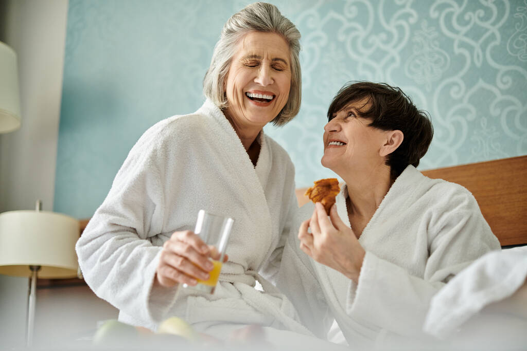 Дві старші лесбійки в білому одязі діляться їжею разом з любов'ю і ніжністю. - Фото, зображення