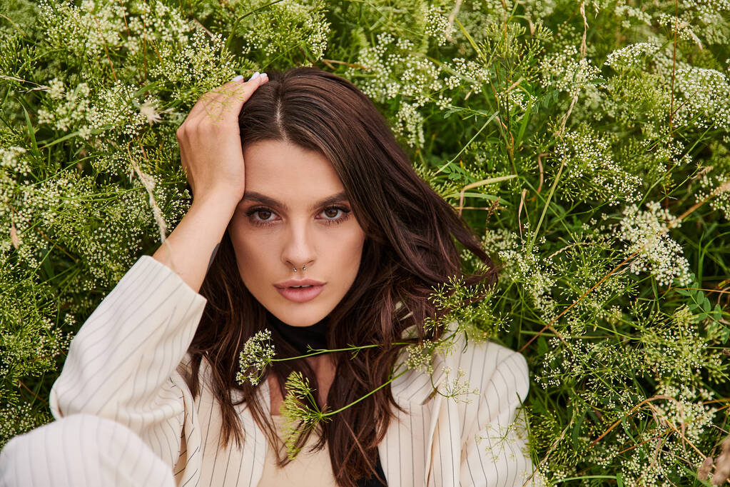 Una giovane donna in abito bianco siede nell'erba con le mani sulla testa, godendo la brezza estiva in un vasto campo. - Foto, immagini