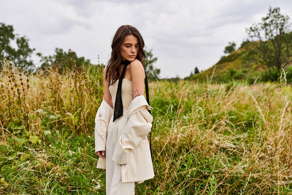 Egy gyönyörű, fehér ruhás fiatal nő áll magasan a magas fű mezején, átölelve a szelíd nyári szellőt.. - Fotó, kép
