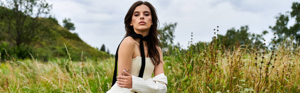 Красива молода жінка в білому вбранні стоїть спокійно на полі високої трави, обіймаючи літній бриз. - Фото, зображення