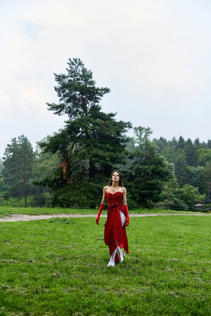 Kırmızı elbiseli ve uzun eldivenli çekici genç bir kadın zarif bir şekilde bir tarlada duruyor yaz esintisini kucaklıyor.. - Fotoğraf, Görsel