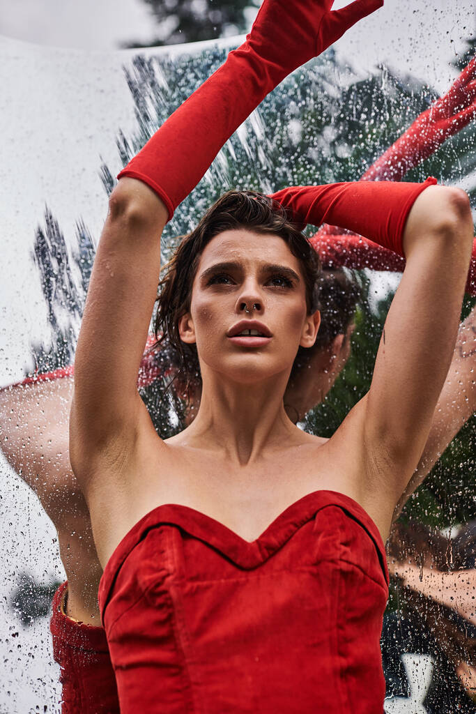 Une femme élégante dans une robe rouge fluide et de longs gants, embrassant la brise d'été dans un cadre naturel. - Photo, image