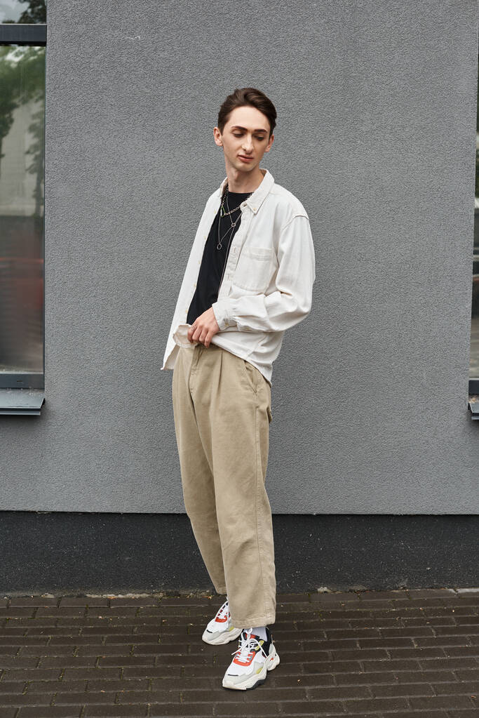 Een jonge homo draagt vol vertrouwen een wit hemd en een bruine broek, en straalt trots en stijl uit.. - Foto, afbeelding