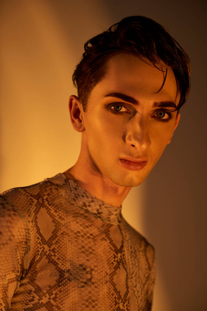 Un giovane uomo che indossa orgogliosamente un top di pelle di serpente, mostrando la sua espressione unica ed elegante di identità queer e orgoglio. - Foto, immagini